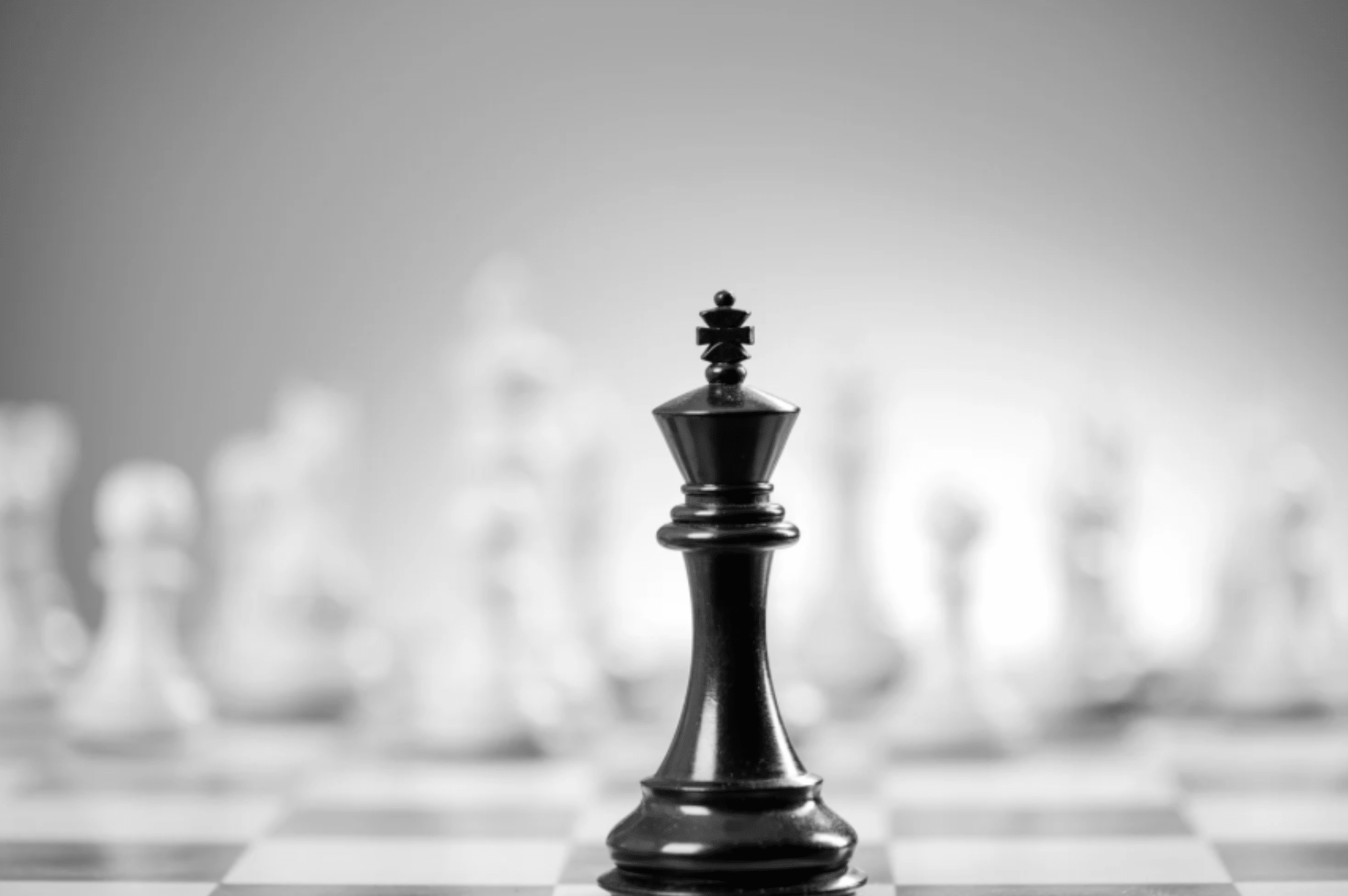 Black chess piece in front of blurred white chess pieces on chess board with gray chess board